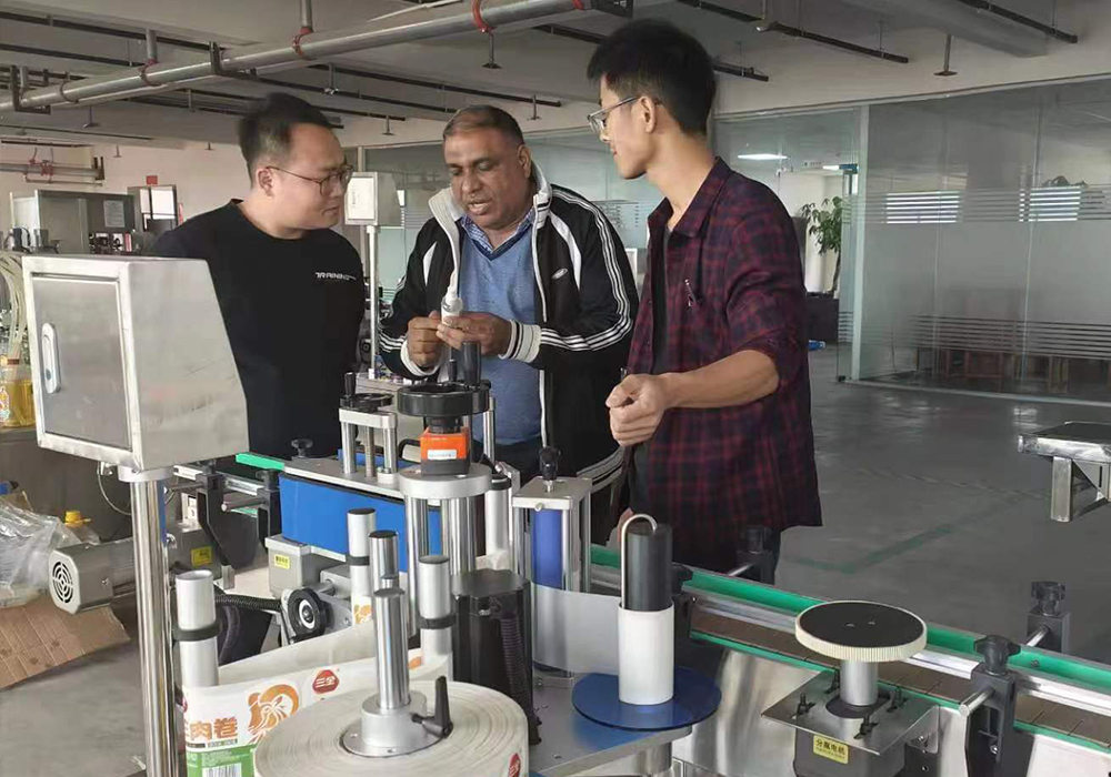 Customer viewing at the factory. He had some questions about the machine. He finally ordered a fully automatic round bottle rolling labeling machine